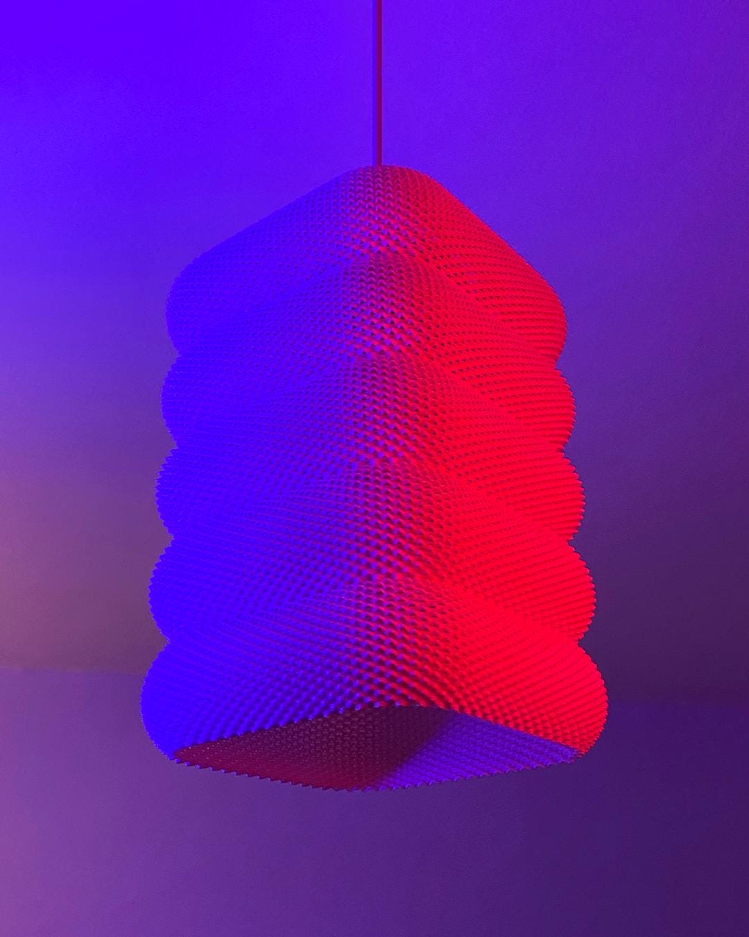 Geometric pendant light with red and blue gradient on a purple background