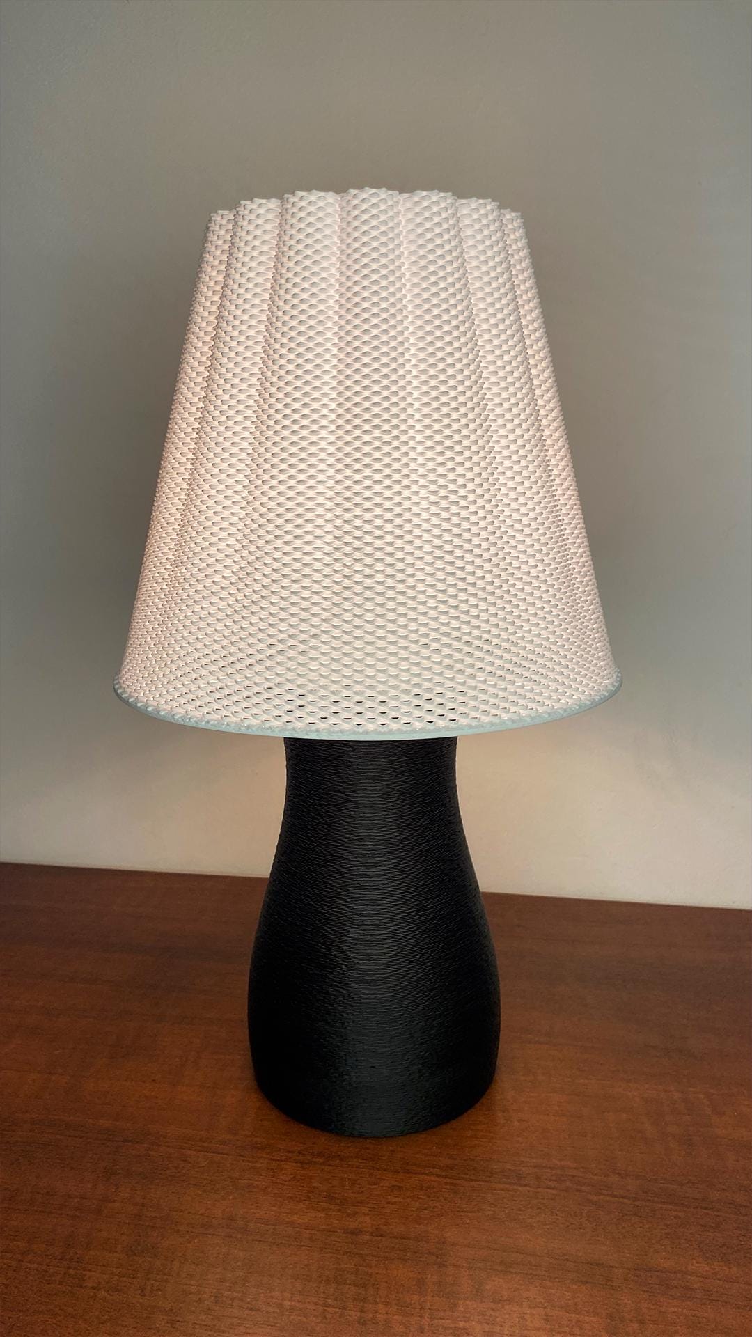 Table lamp with a black base and white textured shade on a wooden surface.