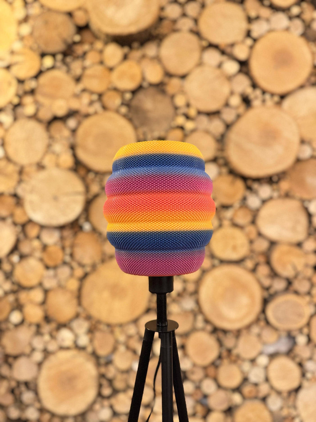 Colorful striped beehive lampshade on a stand against a background of stacked wooden
