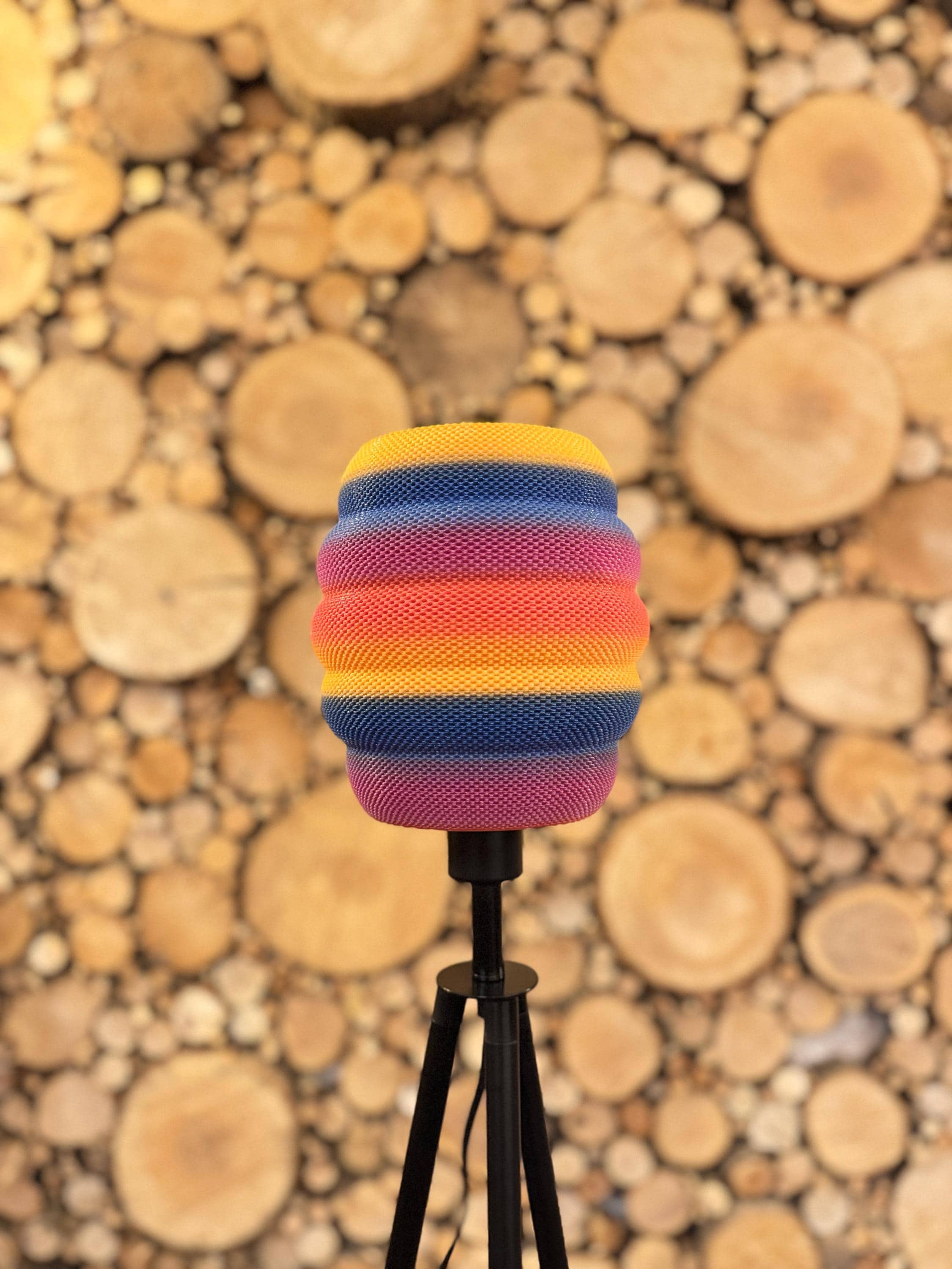 Colorful striped beehive lampshade on a stand against a background of stacked wooden