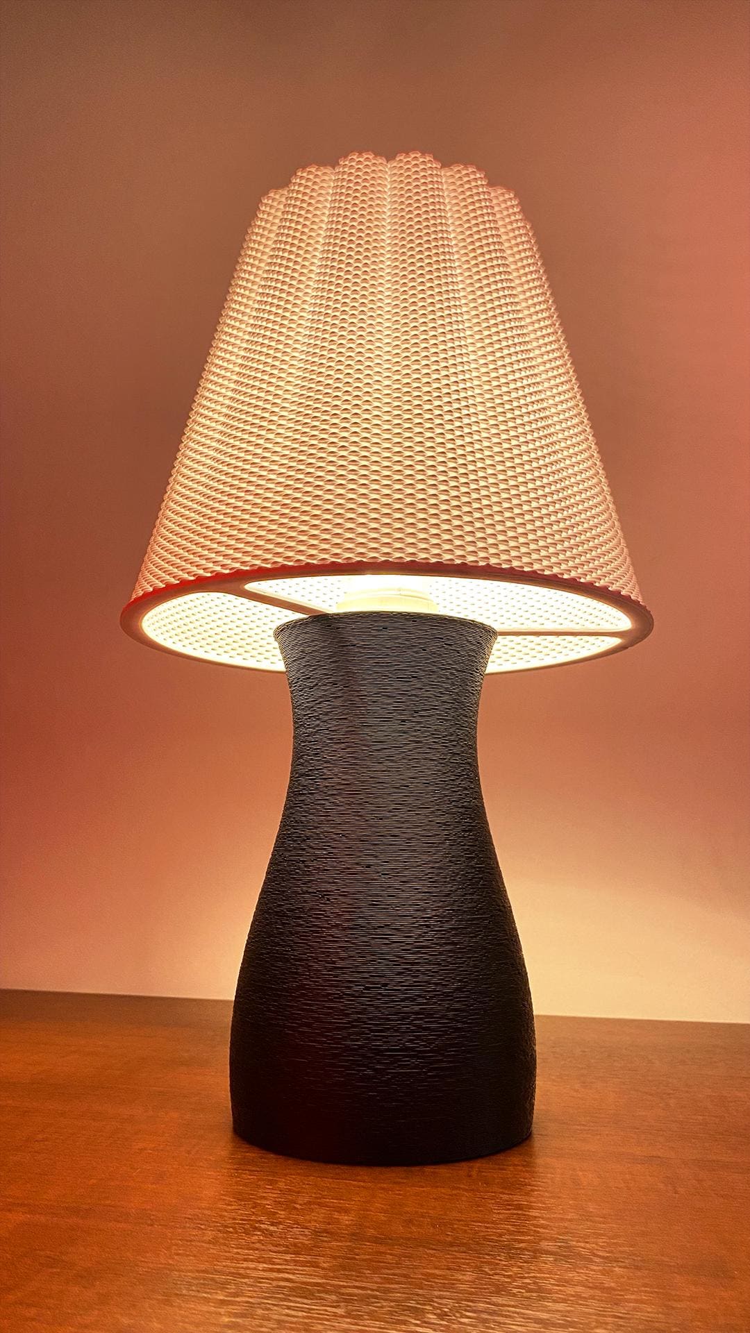 Table lamp with textured black base and white woven shade on a wooden surface.