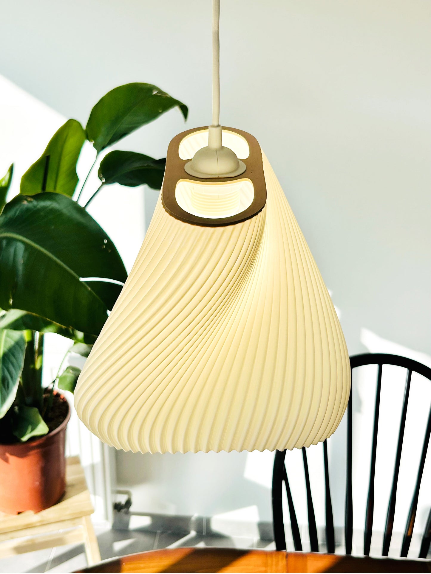 Beige pendant lamp hanging in a room with a plant and chair.