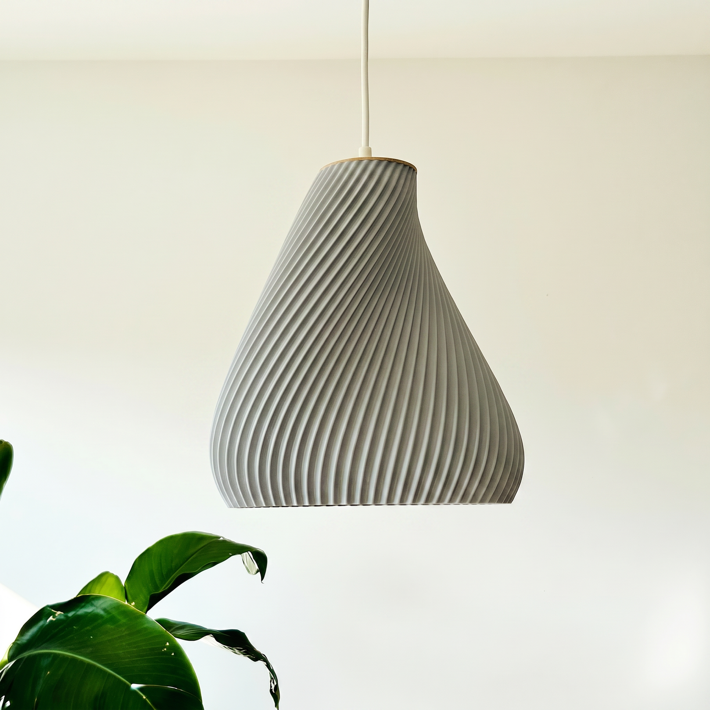 Textured pendant light hanging against a neutral background with a plant in the corner.