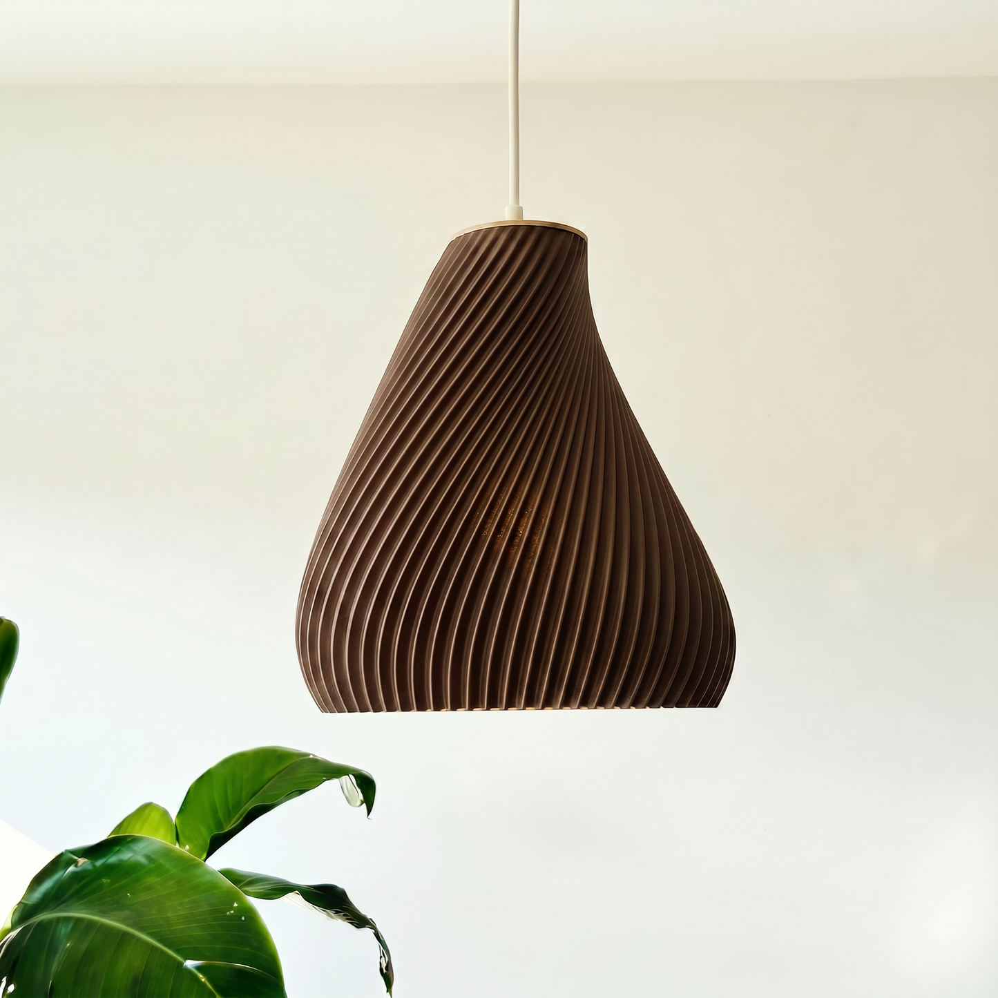 Brown ribbed pendant light hanging against a neutral background with a plant in the corner.