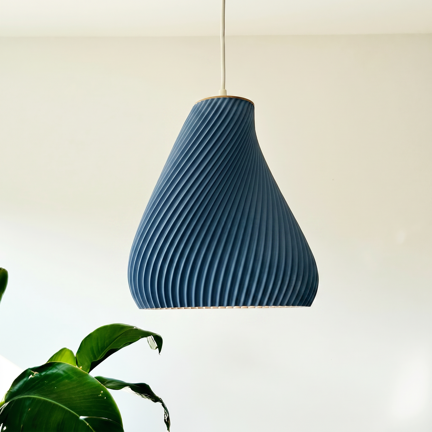 Blue textured pendant light hanging against a plain background with a plant in the corner.