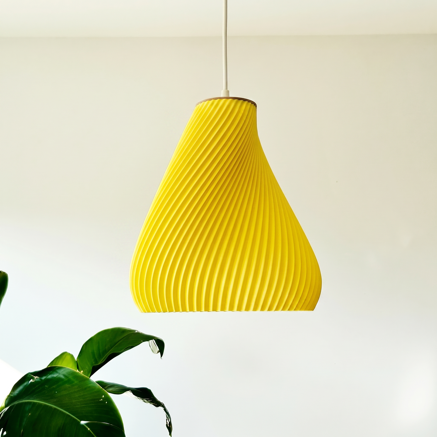 Yellow textured pendant light against a white background with a plant in the corner.