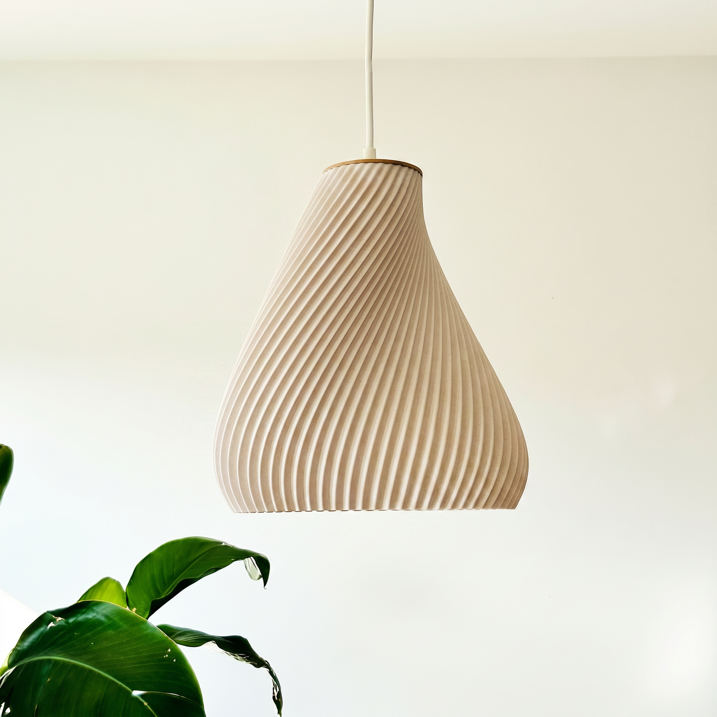 Beige ribbed pendant light against a neutral background with a plant in the corner