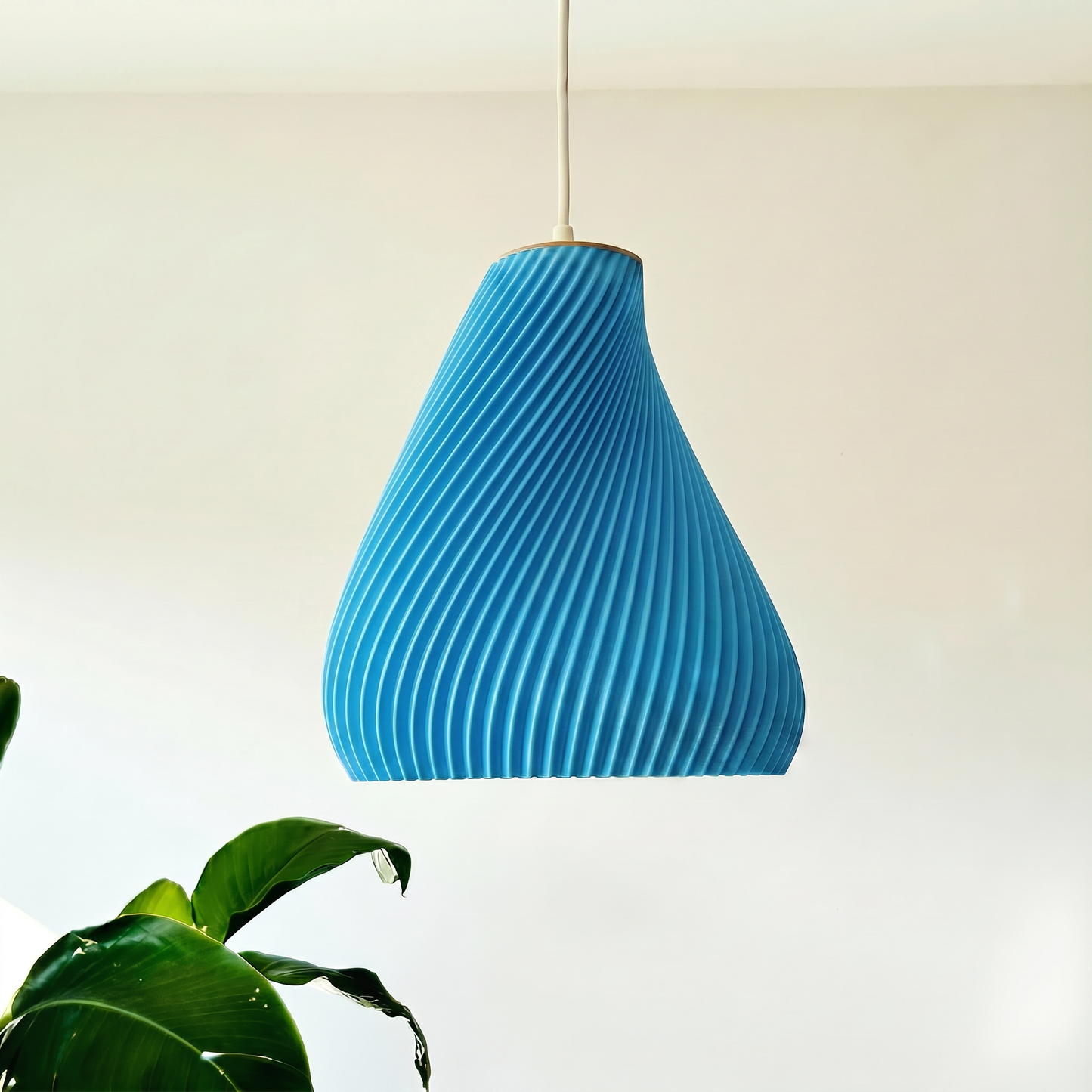 Blue pendant light hanging against a neutral background with a plant in the foreground