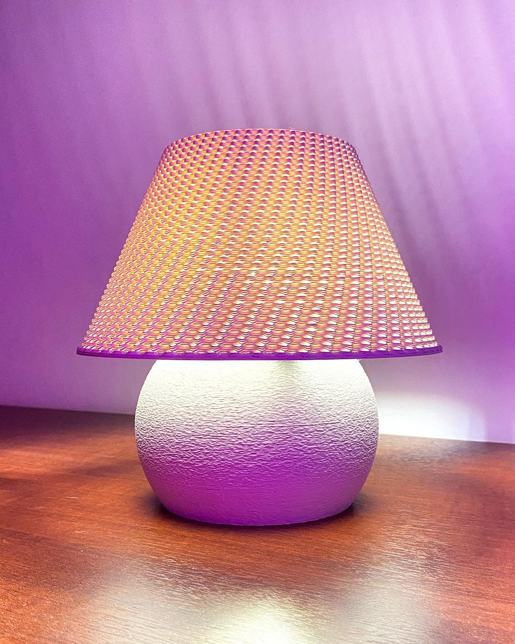 Table lamp with a textured white base and pink woven shade on a wooden surface.