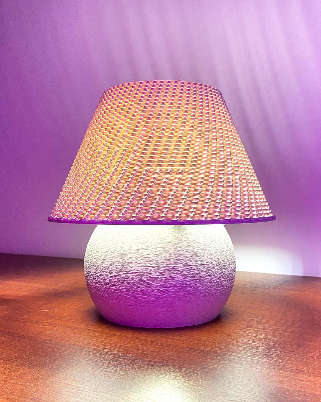 Table lamp with a textured white base and pink woven shade on a wooden surface.
